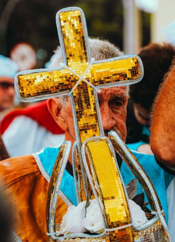 Um devoto leva uma cruz e uma coroa revestidas de espelhos dourados, com rosas brancas