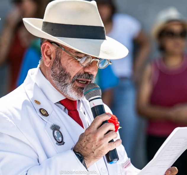 Fernando Guimarães, Presidente da Associação, de terno e chapéu brancos, gravata vermelha e cravo, lê um discurso ao microfone