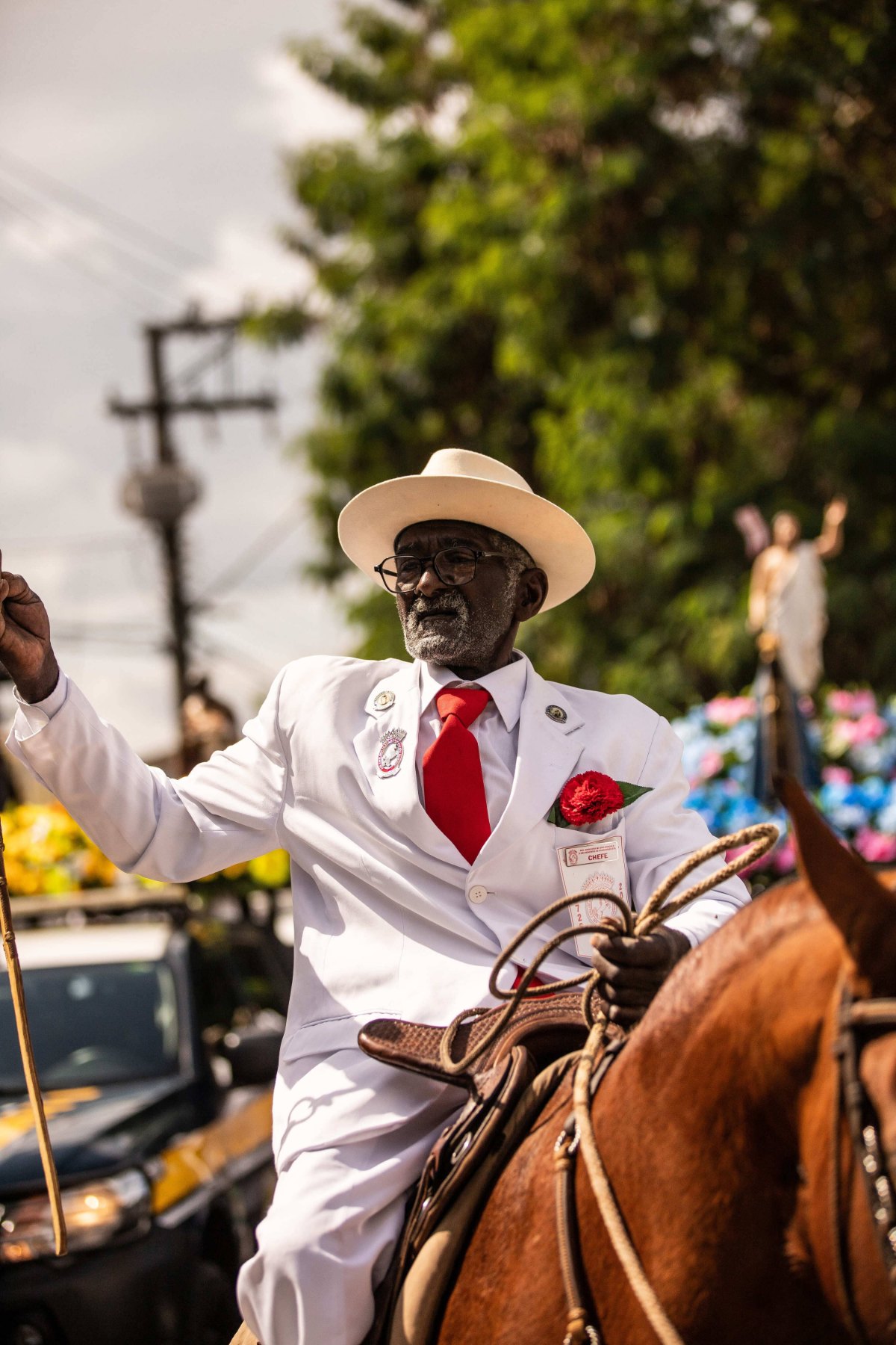 Geraldo Terra, Chefe de Honra da Cavalaria, de terno e chapéu brancos, gravata e cravo vermelhos, a cavalo, com o braço erguido durante o cortejo