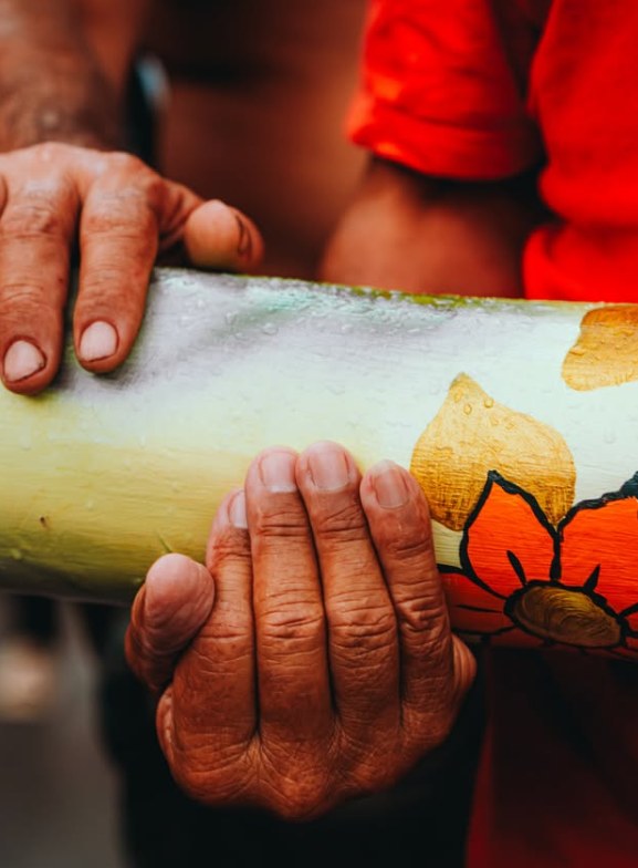 Mãos de devotos seguram o mastro pintado com flores vermelhas e douradas